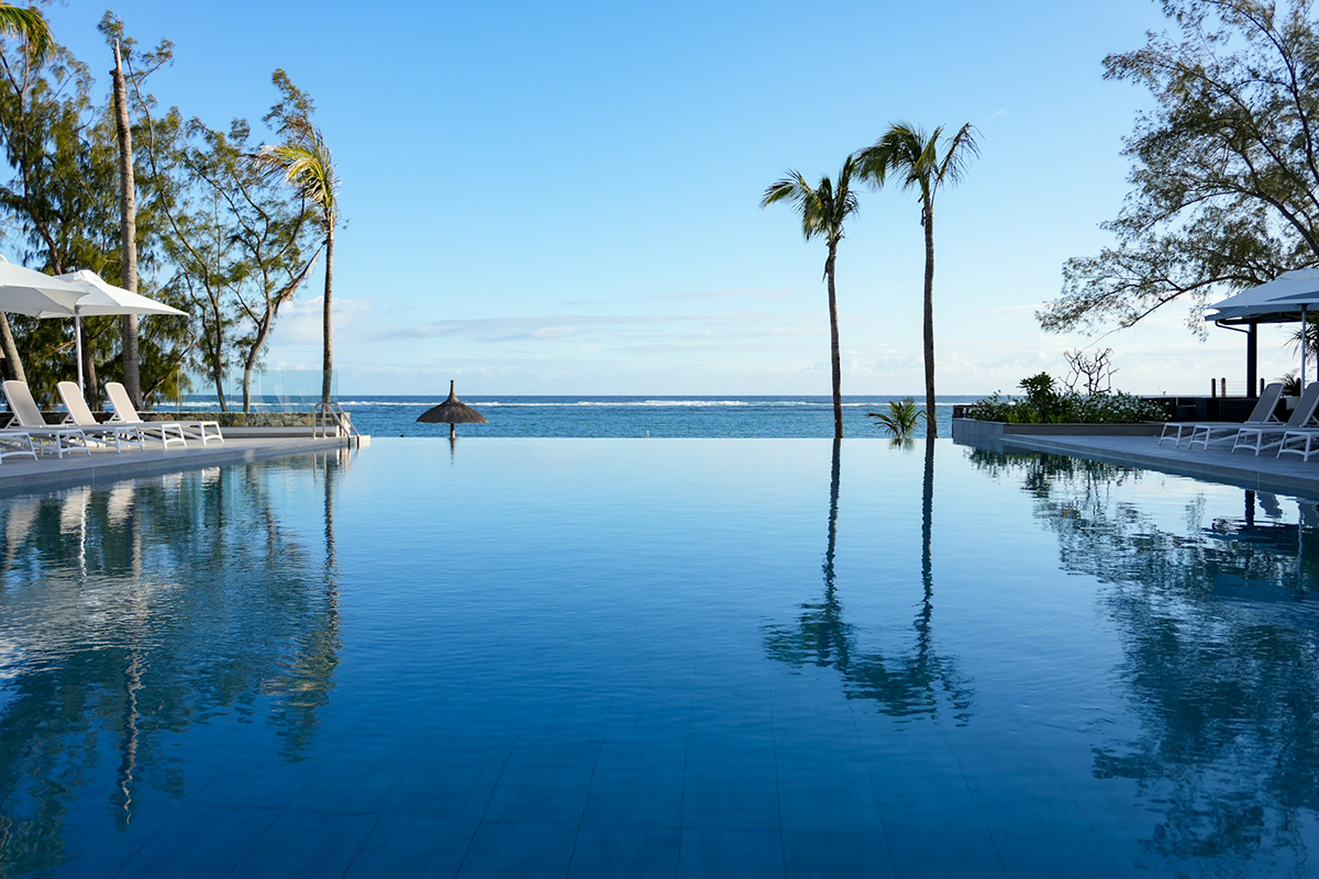Infinity pool at a beach resort looking out to the ocean, with palm trees and lounge chairs