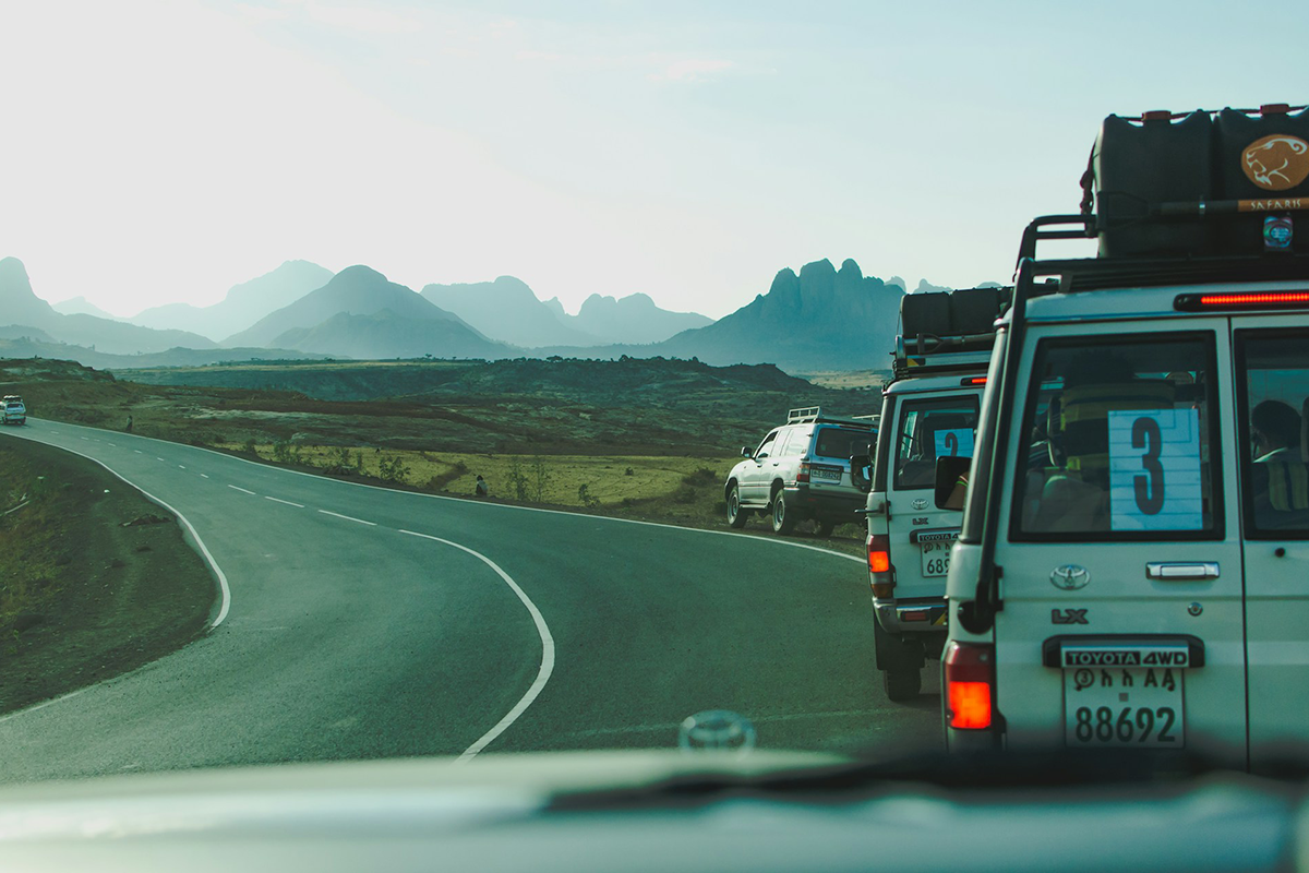 Line of four-wheel-drive tour vehicles on a winding road toward rugged mountains