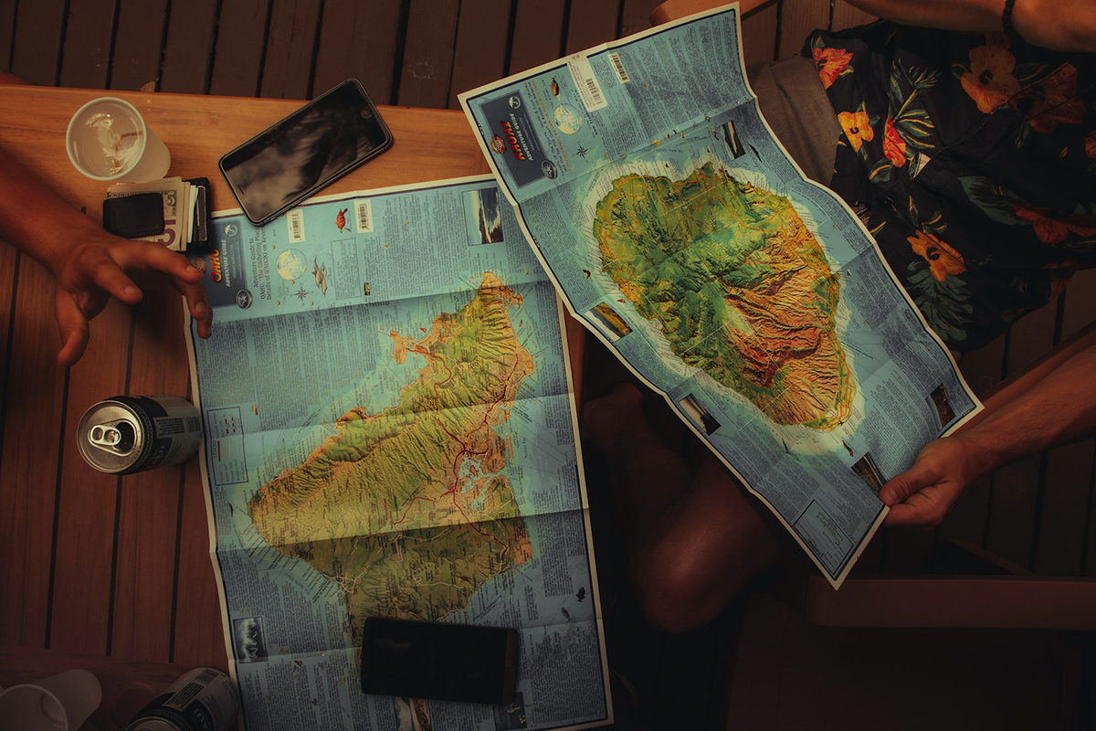 Two island maps spread across a wooden table during trip planning