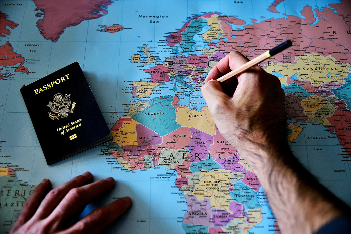 U.S. passport on a world map while a hand marks a route with a pencil